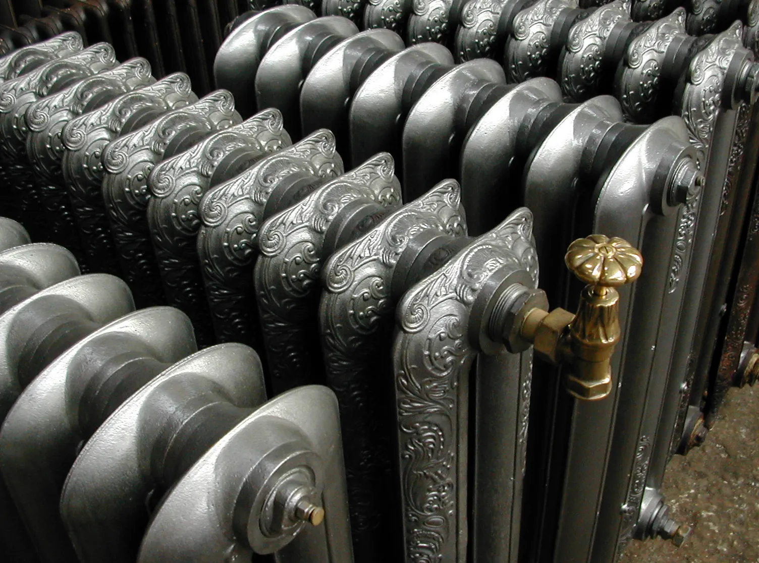 Motifs d’un radiateur en fonte gris et détail de sa robinetterie en laiton